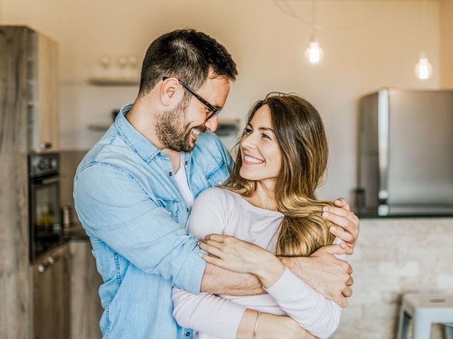 Wohnung mit Bauteilaktivierung Kimaaktiv zertifiert Verliebtes Paar in Umarmung steht in Wohnung, beide lächeln sich vertraut an Hübl und Partner Wohnungen Eigentumswohnungen Vorsorge und Anlage Wohnungen Wien Paar glücklich